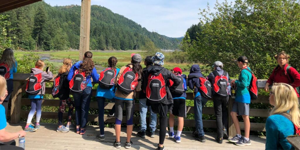 A row of heritage fair student delegates with their sponsored backpacks are looking at a park.